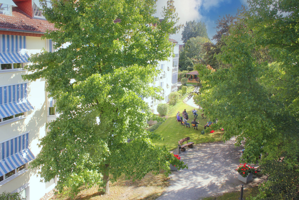 Blick in den Park auf viel Grün, Bänke, Blumen und ein Gruppe Menschen