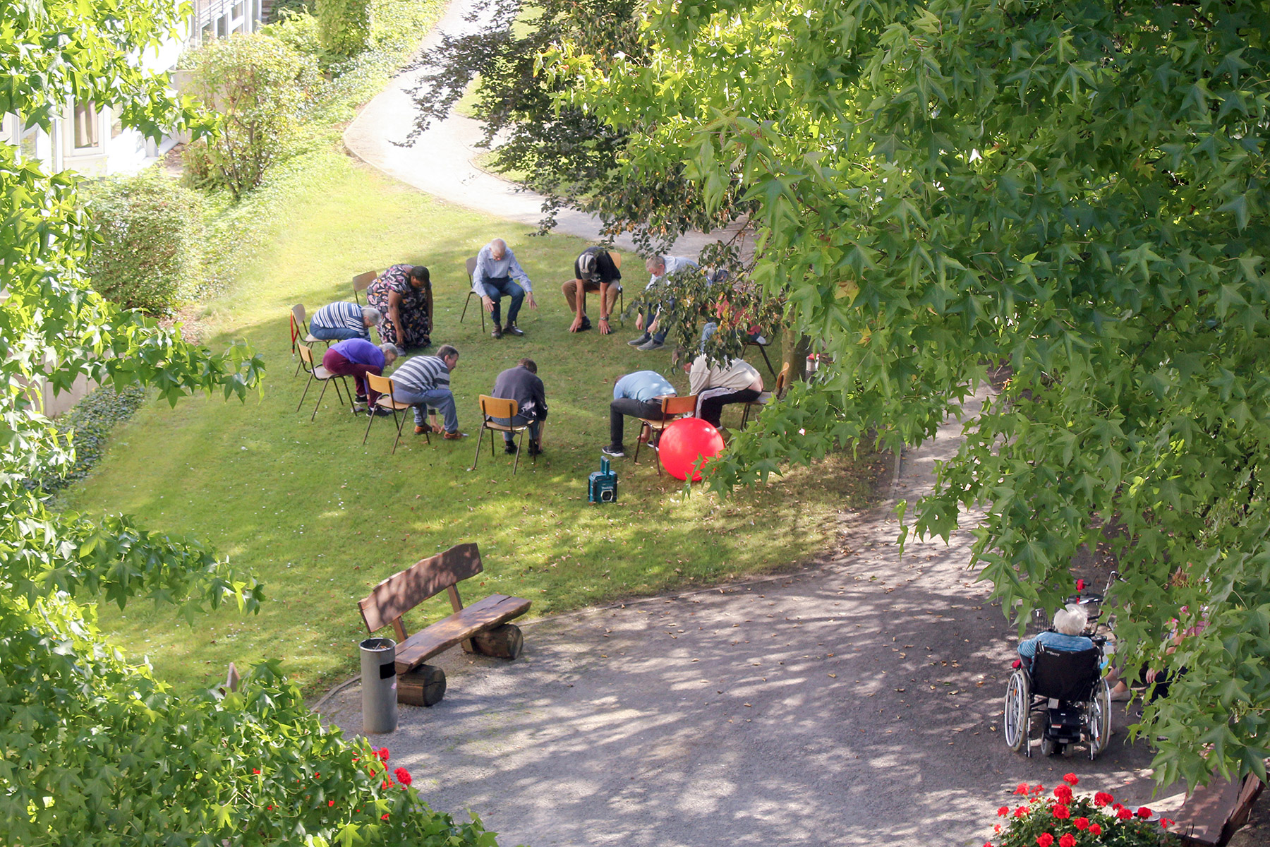Gruppe von Menschen sitzt im Kreis auf Stühlen im Freien und macht gemeinsam Therapieübungen auf einer Wiese