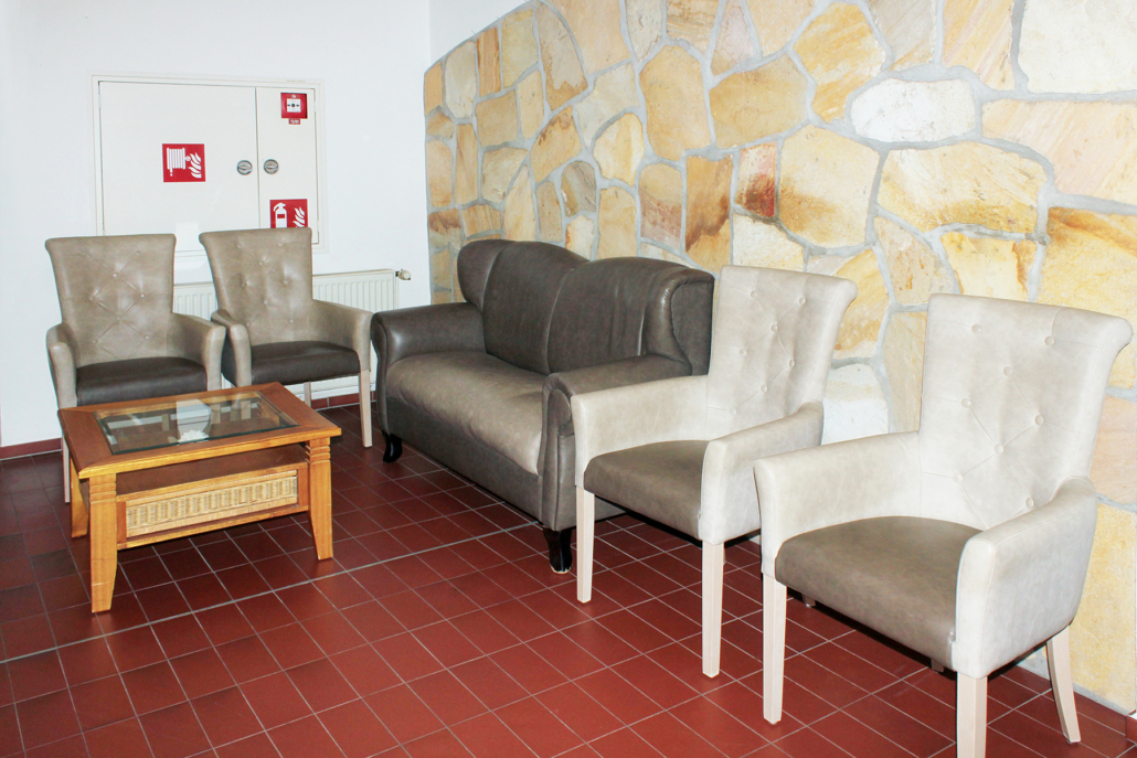 Ruhebereich mit Sesseln, dunklerLedercouch und einem Holztisch vor einer Steinwand