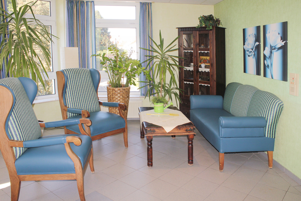 Ruhebereich im Flur mit zwei blauen Sesseln, blauem Sofa, Holztisch mit Pflanzen und edlem Schrank mit Glasfront
