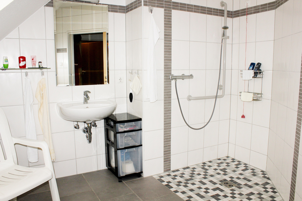 Helles Badezimmer mit Waschbecken, Spiegel, Ablage, begehbarer Dusche und Stuhl